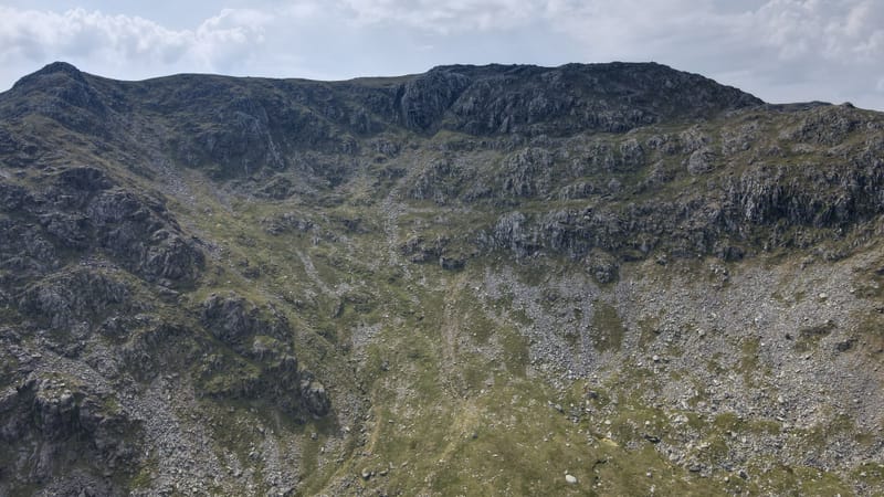 A steep rock face and scree slope on the side of a mountain, seen from the air.
