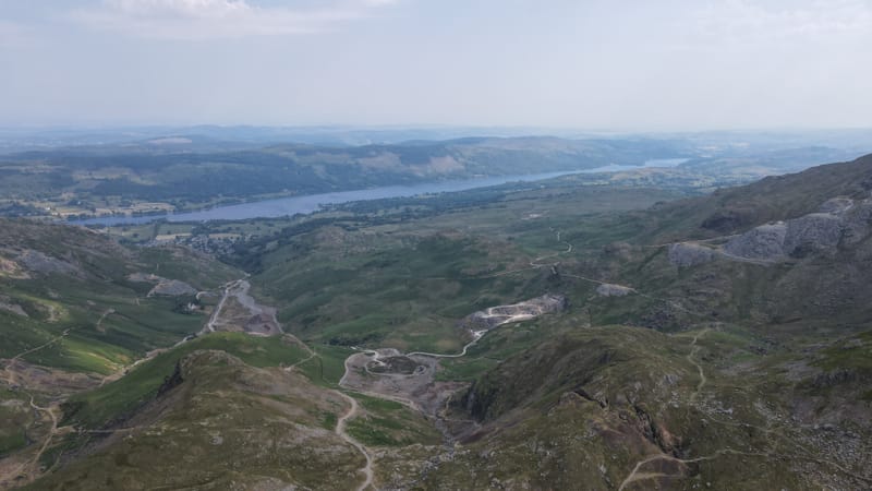 A green valley winding down to a long lake, with tracks and old spoil heaps on the hillside.